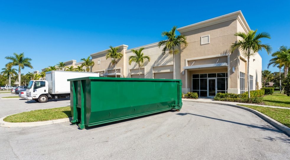 Green dumpster in front of a commercial building with palm trees in Southwest Florida